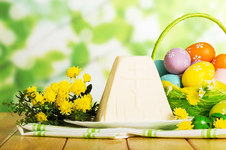 Colored Easter eggs in a basket the traditional Easter cheese dessert, cloth napkin, flowers, herb, abstract green background.の写真素材
