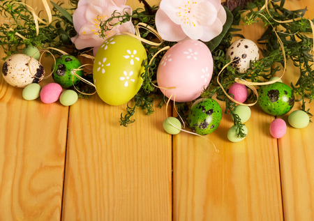 Colored Easter eggs, branch with flowers, candy and ribbon against the backdrop of pale wood.の写真素材