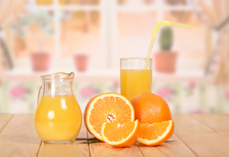 Jug and glass of fresh orange juice with a straw, orange, half and slices on the kitchen background.の写真素材
