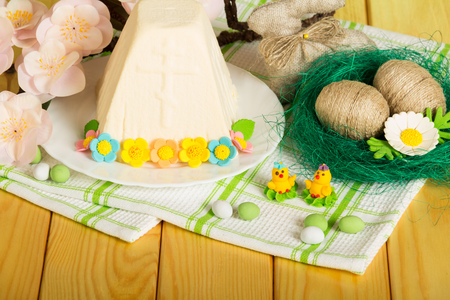 Easter cheese dessert on a plate decorated with flowers, Easter eggs wrapped with twine in the nest, Easter Bunny, toy chickens and candy on a background of light wood.の写真素材