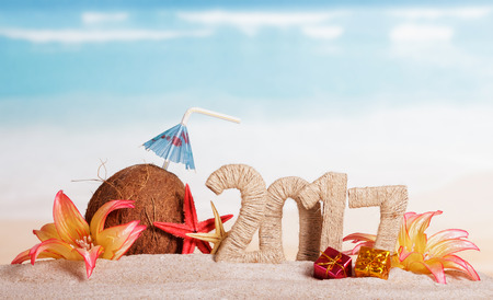 Figures 2017 twined with twine, coconut with a straw and the umbrella of, sea stars, gifts and flowers in the sand against the sea.の写真素材