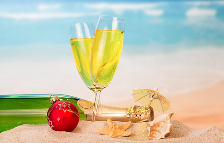 Bottle and two glasses of champagne, Christmas ball, umbrella, a starfish and a seashell in the sand on the sea background.の写真素材