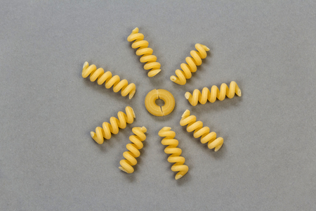 Spiral and curved pasta, laid out in the form of the sun with rays on a gray background.の写真素材