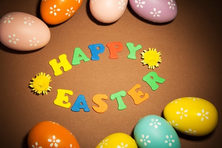 Colored Easter eggs, Happy Easter inscription and flowers on a brown background.の写真素材