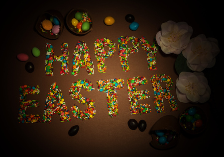 Inscription Happy Easter, built of colorful flouring for Easter, candy, flowers on a brown background.の写真素材