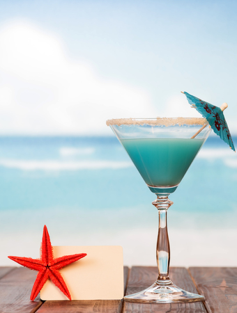 Cocktail with umbrella, blank card and starfish on the background of the sea.の写真素材