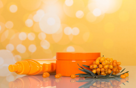 Branch with berries of sea buckthorn, a jar of cream and bottle of gel on abstract yellow background.の写真素材