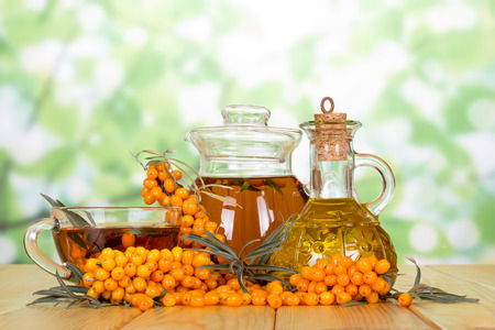 Branch with berries of sea buckthorn, oil bottle and tea on abstract green background.の写真素材