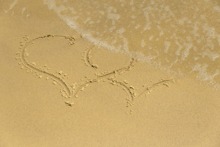 Sea foam washes the symbol of two hearts on the sandの写真素材