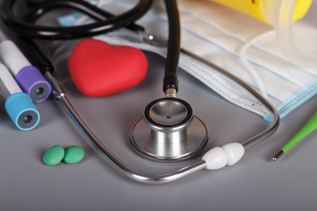 Medical stethoscope, pills, heart, vacuum tube, a thermometer and a mask on a grey background.の写真素材