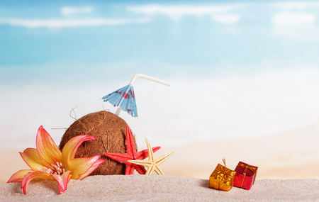 Coconut with drinking straw and umbrella, gifts, starfish and flower on the sand.の写真素材