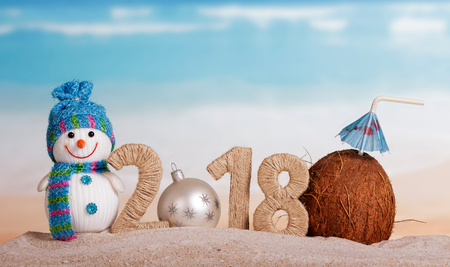 New Year inscription 2018, white Christmas ball instead of the number 0, a snowman and coconut with a straw in the sand at the beach.の写真素材