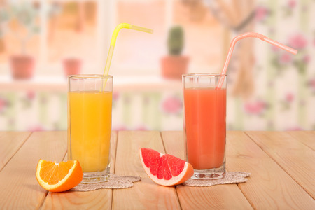 Two glasses of fresh orange and grapefruit juices, straws and pieces of fruit on the background of the kitchen.の写真素材