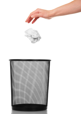 Empty shopping basket for paper waste and a female hand throws a ball out of crumpled paper isolated on white background.の写真素材
