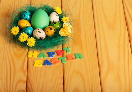 Colorful Easter eggs in the nest and the inscription HAPPY EASTER on a light board.の写真素材
