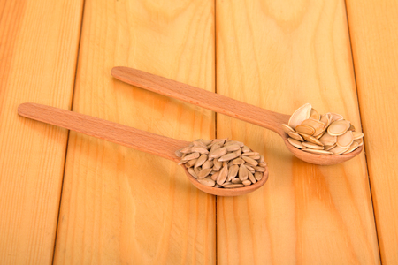 Wooden spoons with pumpkin seeds and peeled sunflower seeds on a light wood background.の写真素材