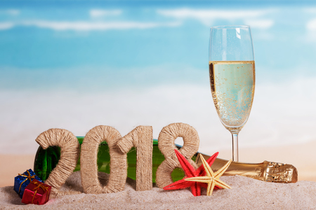New Year inscription 2018, a bottle and a glass of champagne, gifts, starfish in the sand on the beach.の写真素材