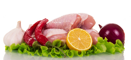 Raw chicken legs, onion, hot pepper, garlic, part of lemon and lettuce leaves isolated on white background.の写真素材