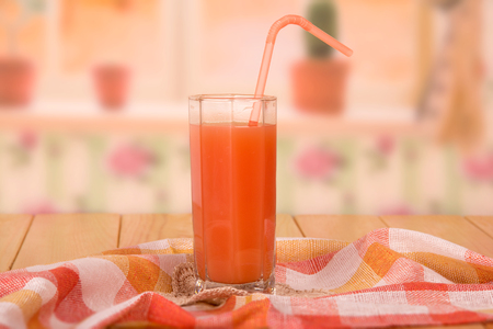 A glass of fresh grapefruit juice with a straw, towel, and lace napkin on kitchen background.の写真素材