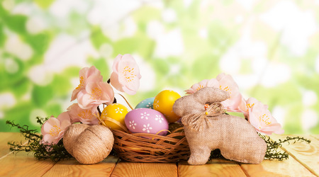 Are different Easter eggs in a basket and near, the Easter Bunny, a branch with flowers on the abstract green background.の写真素材