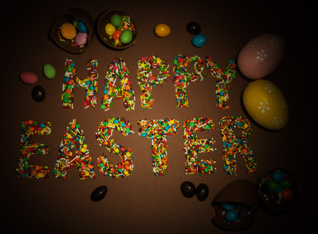 Inscription Happy Easter, built of colorful flouring for Easter, Easter eggs and sweets on a brown background.の写真素材