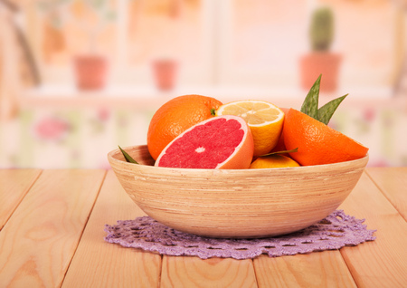 Whole and sliced grapefruits, lemons and oranges with leaves in a bowl close-up on the kitchen background.の写真素材
