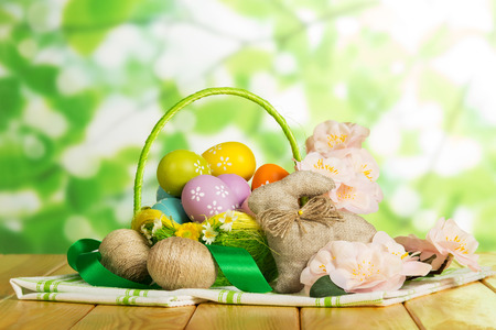 Colored Easter eggs in a basket next to the two intertwined cords, easter bunny, flowers and ribbons on the abstract green background.の写真素材