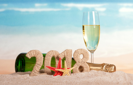New Year inscription 2018, a bottle and a glass of champagne, starfish on the sand.の写真素材