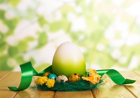 Colorful Easter eggs in the nest, one large and ribbon on abstract green background.の写真素材