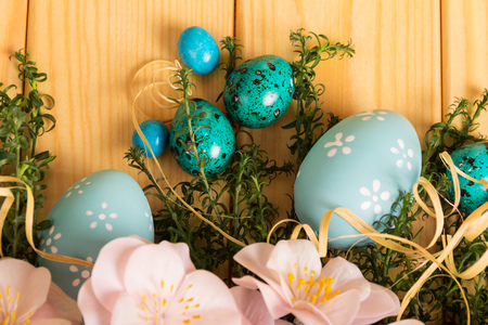 Various Easter eggs, dragees, flowers, herbs and ribbon against the backdrop of pale wood.の写真素材