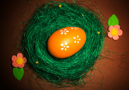 The nest, lined with grass with Easter eggs and flowers on a brown background.の写真素材