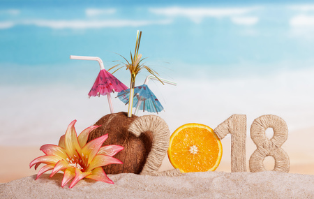 New Year inscription 2018, half of the orange instead of the numbers 0, coconut with straws and flower in the sand.の写真素材