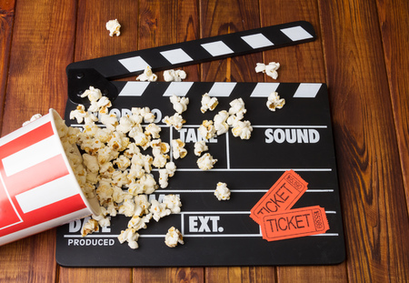 Black with white letters party poppers, a box of spilled popcorn and movie tickets on a background of dark wood.の写真素材