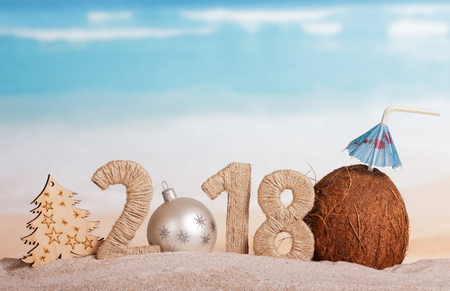 New Year inscription 2018, white Christmas ball instead of the number 0, the tree and the coconut with a straw in the sand at the beach.の写真素材