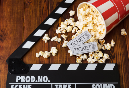 Spilled popcorn, striped box, movie tickets and movie clapper against the dark wood.の写真素材