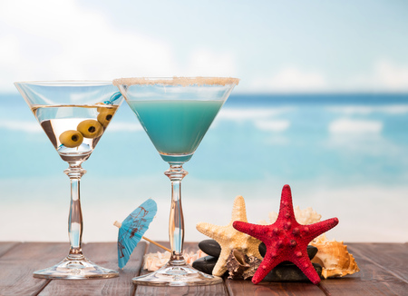 Cocktail, umbrella, alcohol with olives, starfish, smooth stones and sea shell on the background of the sea.の写真素材