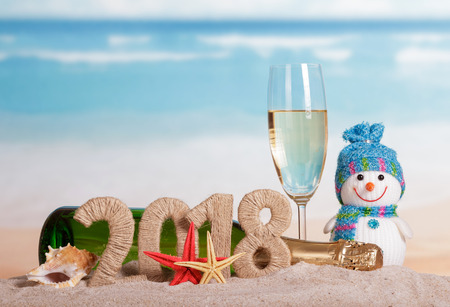 New Year inscription 2018, a bottle and a glass of champagne, snowman, starfish and seashell in the sand.の写真素材