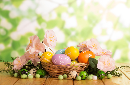 Colorful Easter eggs in a basket and near, candy, grass, branch with flowers on the abstract green background.の写真素材