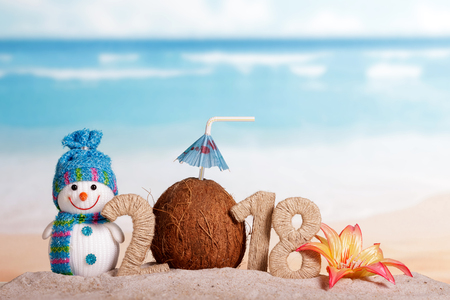 New Year inscription 2018, coconut with drinking straw and umbrella instead of the number 0, a snowman, a flower in the sand on the beach.の写真素材