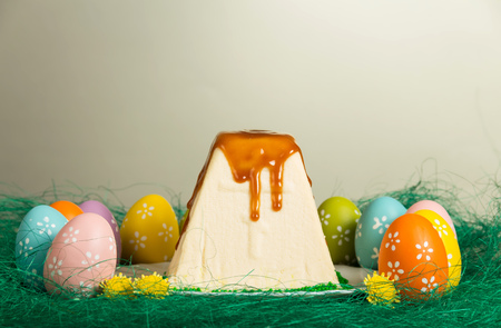 Traditional Easter curds dessert on a plate watered glaze, colored easter eggs, flowers and grass is laid out in the form of nests on a gray backgroundの写真素材
