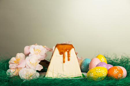 Traditional Easter curds dessert watered glaze, colored easter eggs, branch with flowers and grass is laid out in the form of nests on a gray background.の写真素材