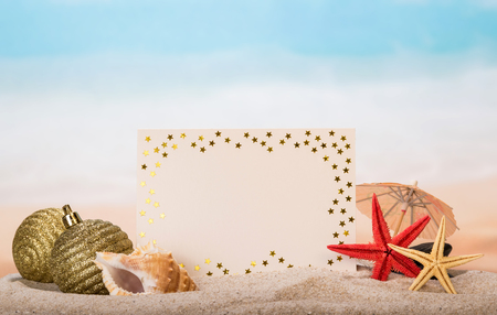 A blank card, an umbrella, Christmas balls, starfish and a sea shell in the sand against the sea.の写真素材