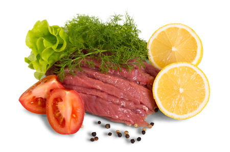 Pieces of raw beef, pepper, slices of lemon and tomato, salad, dill, isolated on white background.の写真素材