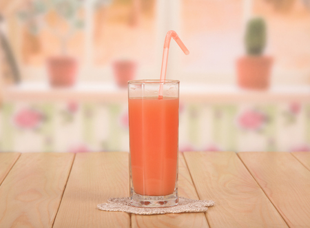 A glass of fresh grapefruit juice with a straw and lace napkin on kitchen background.の写真素材