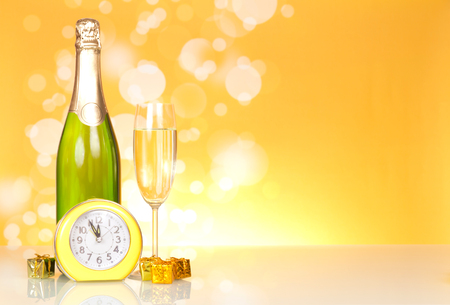 Bottle with champagne, small New Year surprises and clock on yellow backgroundの写真素材