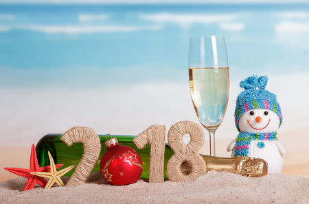 New Year inscription 2018, the Orb instead of the number 0, a bottle and a glass of champagne, snowman, starfish on the sand.の写真素材