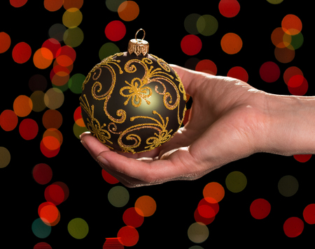 Beautiful Christmas toy-ball with patterns in woman's hand, on dark sparkling backgroundの写真素材