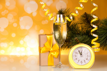 Champagne, spruce branch, box with gift on sparkling yellow backgroundの写真素材