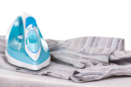 Electric iron and clean laundry, on an ironing board, isolated on white backgroundの写真素材
