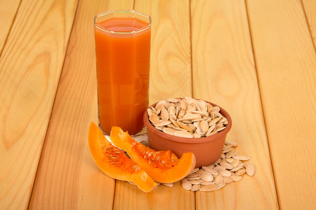 Pumpkin pieces, a glass of pumpkin juice, a bowl with pumpkin seeds and next to a light wood background.の写真素材